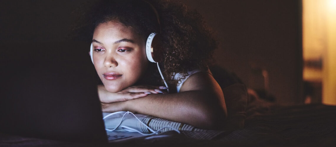 Young woman wearing headphones binge-watching a show on her laptop.